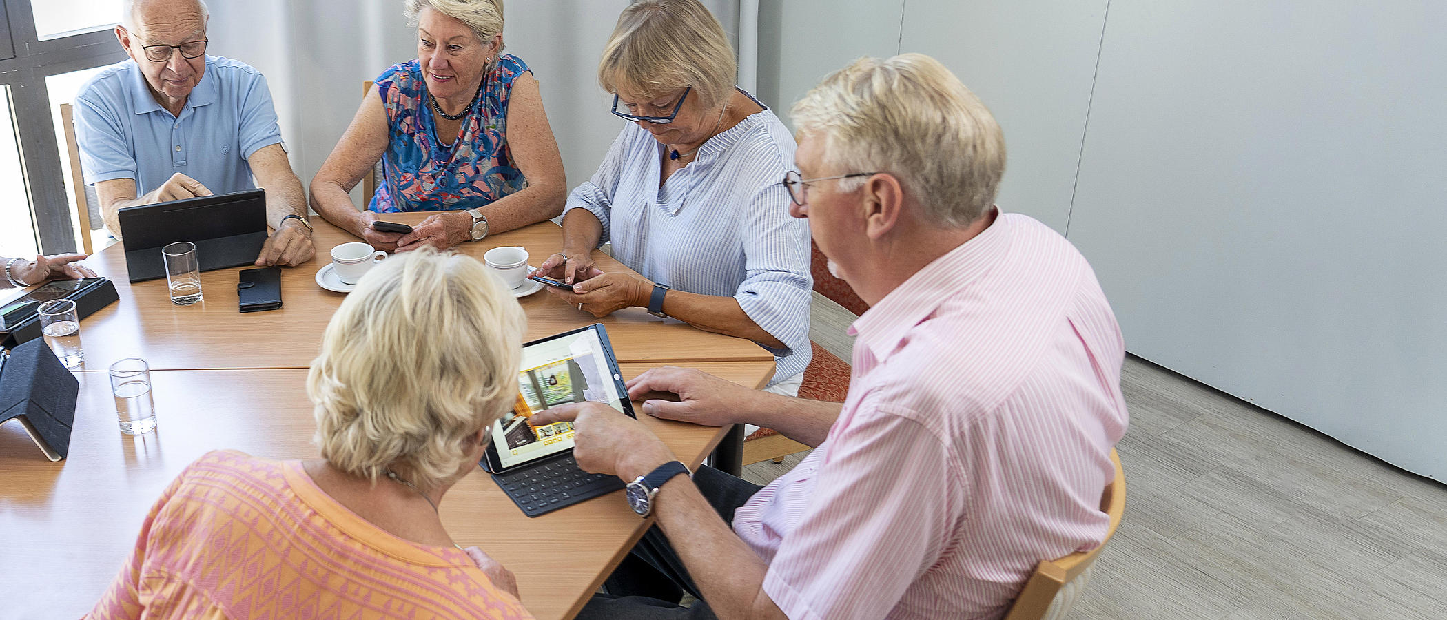 Eine Gruppe älterer Menschen sitzt mit Tablets an einem Tisch. 