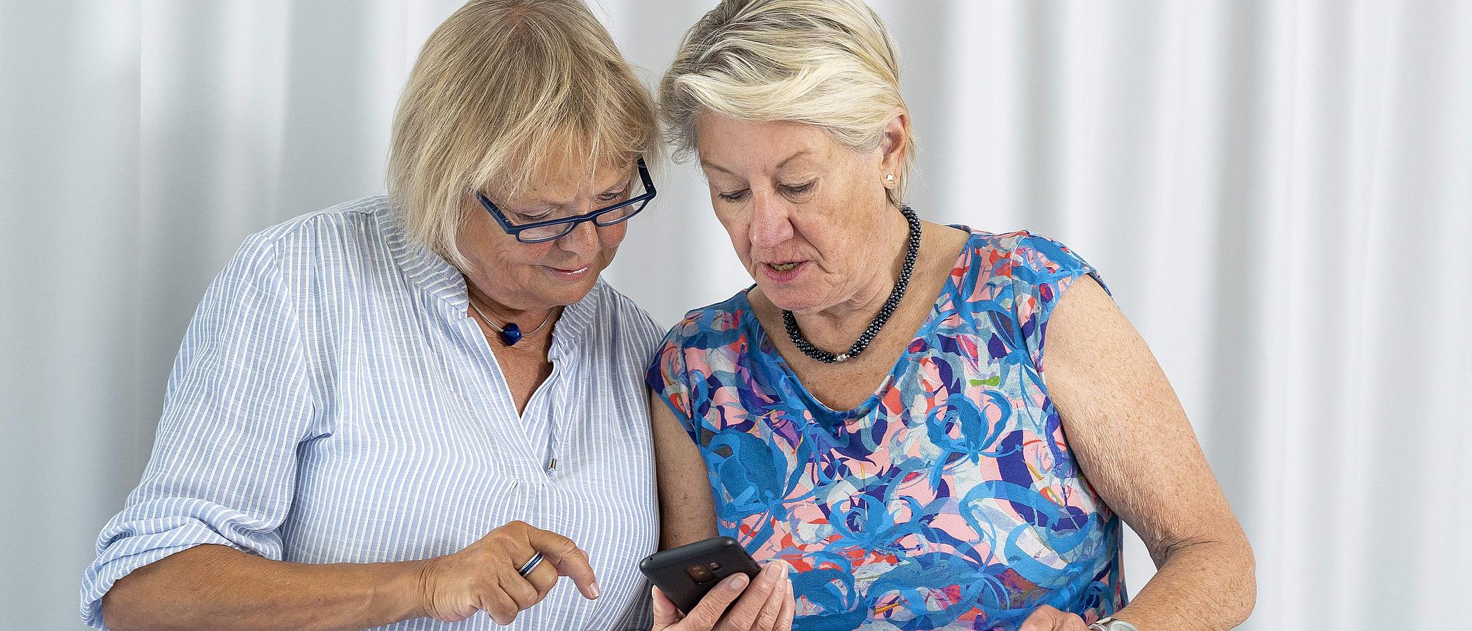 Zwei Frauen schauen gemeinsam auf ein Smartphone. 